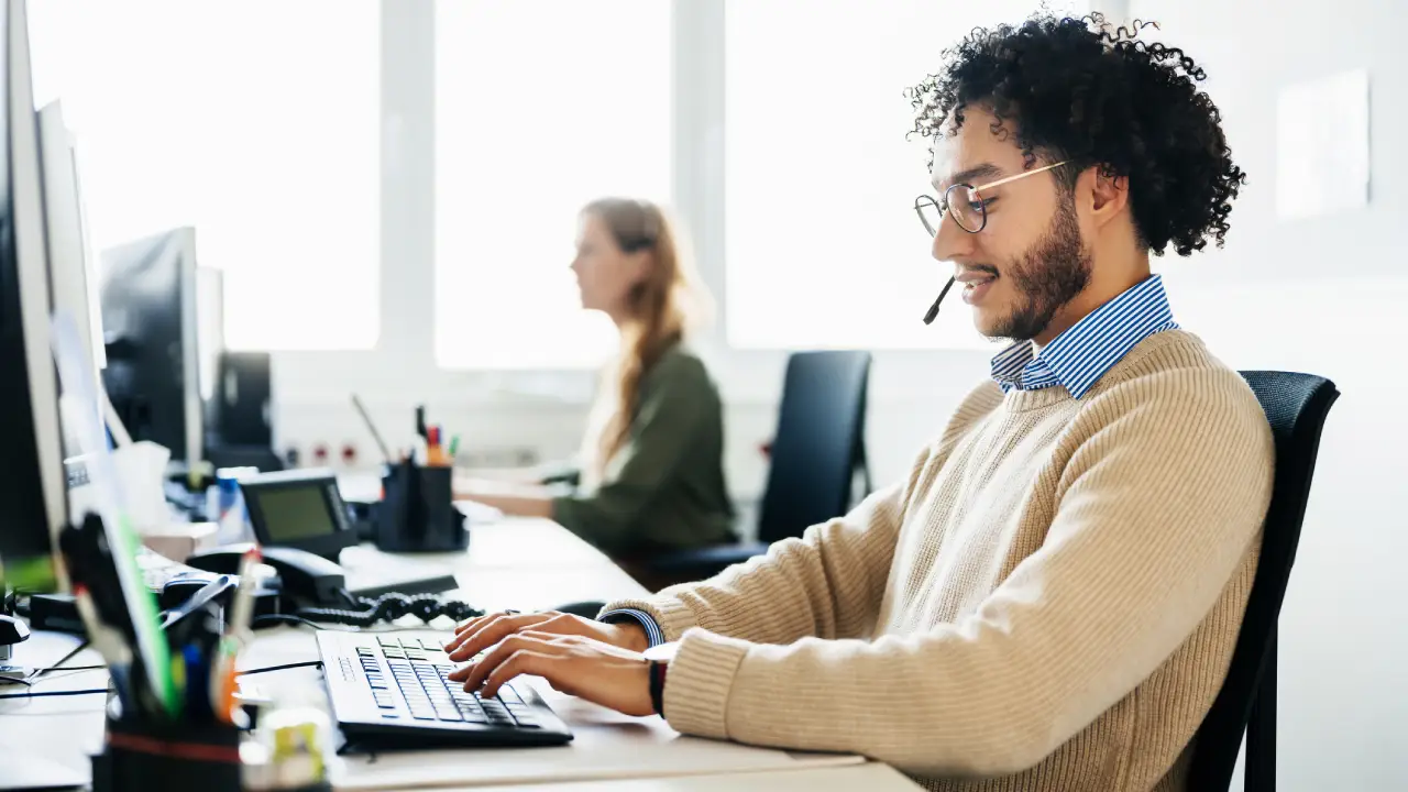 A bank customer service representative in a modern office looking at a desktop computer screen while taking a call, realistic photography style