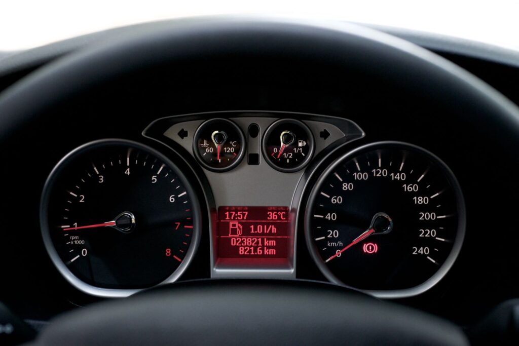A close-up of a car odometer and dashboard while driving on a highway during a daytime road trip, realistic photography style