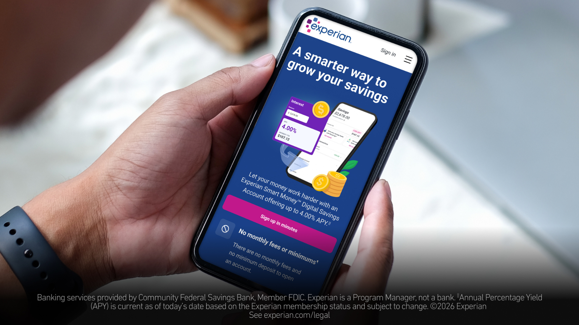 A close-up photo of a person holding a smartphone showing a savings account balance screen while sitting at a desk, realistic banking photo