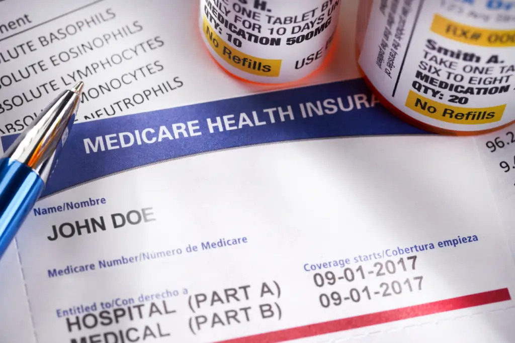 A close-up photo of prescription bottles and a Medicare-related paper on a pharmacy counter with a payment terminal nearby