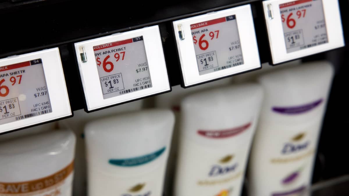 A close-up photo of retail shelf price tags with sale stickers on products in a store aisle, realistic photography