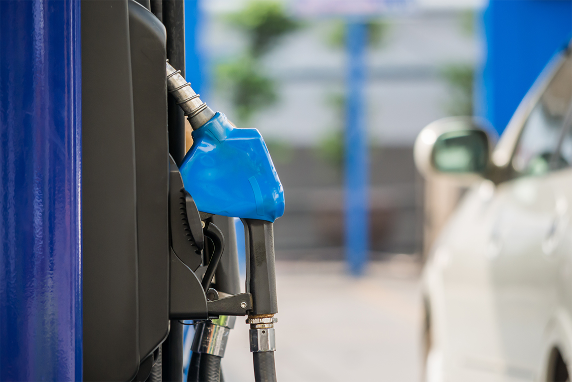 A close-up photograph of a gas station pump with a credit card reader and fuel nozzle visible, suggesting higher energy costs and inflation pressure