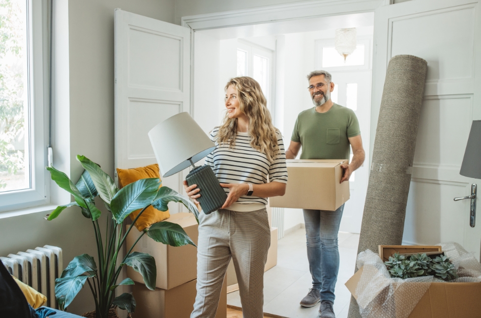 A couple carrying moving boxes through the front door of a new home, natural light, candid lifestyle photo