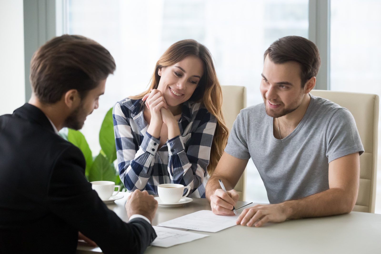 A couple sitting across from a mortgage lender in a small office reviewing documents together, realistic photography