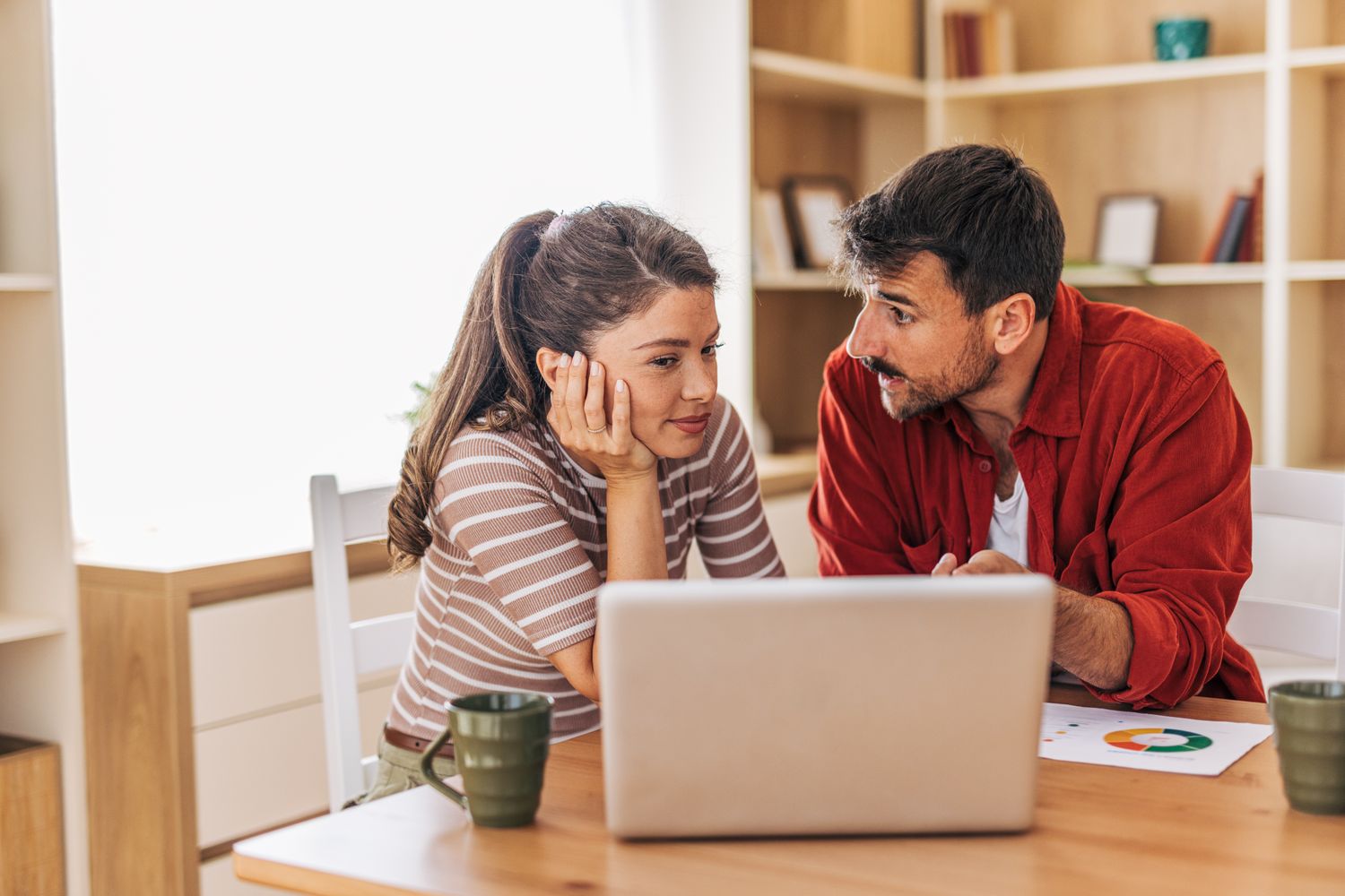 A couple sitting on a couch looking at a laptop displaying a mortgage rate page while taking notes on a notepad, realistic home photo