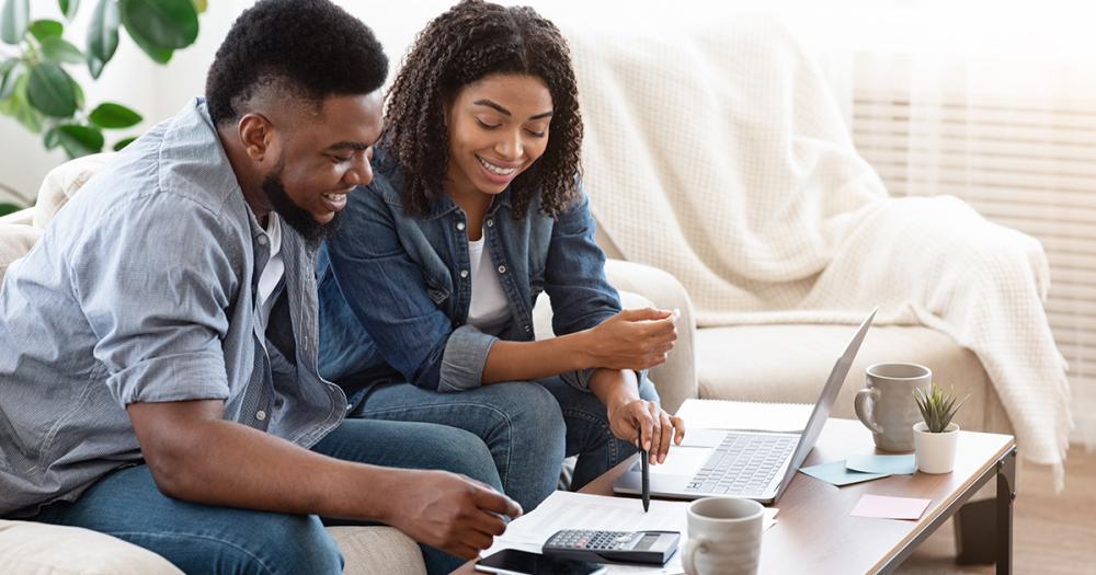 A couple sitting on a couch reviewing their bank account on a laptop together, realistic photo style