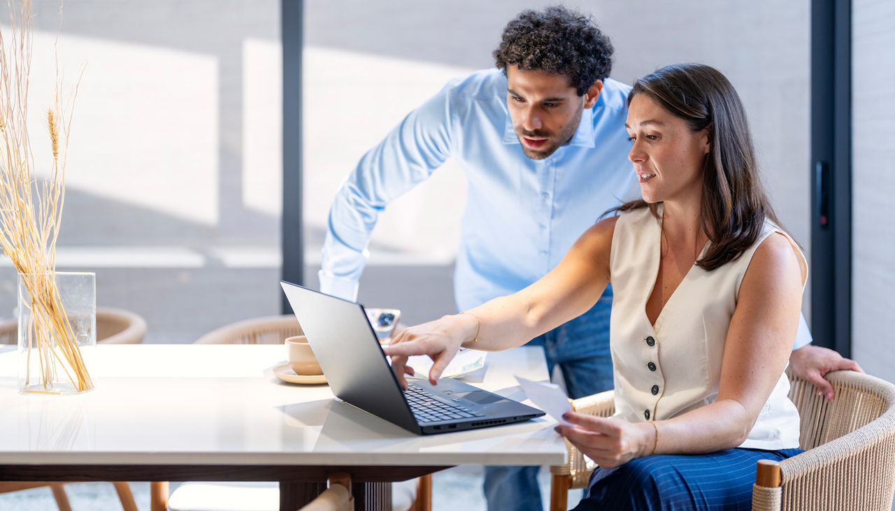 A couple sitting on a living room couch reviewing a monthly budget on a laptop with car paperwork on a coffee table, warm indoor photography style