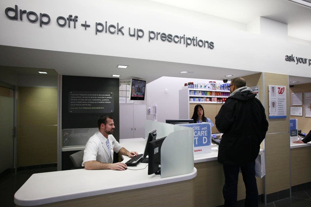 A customer holding a prescription bag while standing at a pharmacy counter with shelves blurred in the background