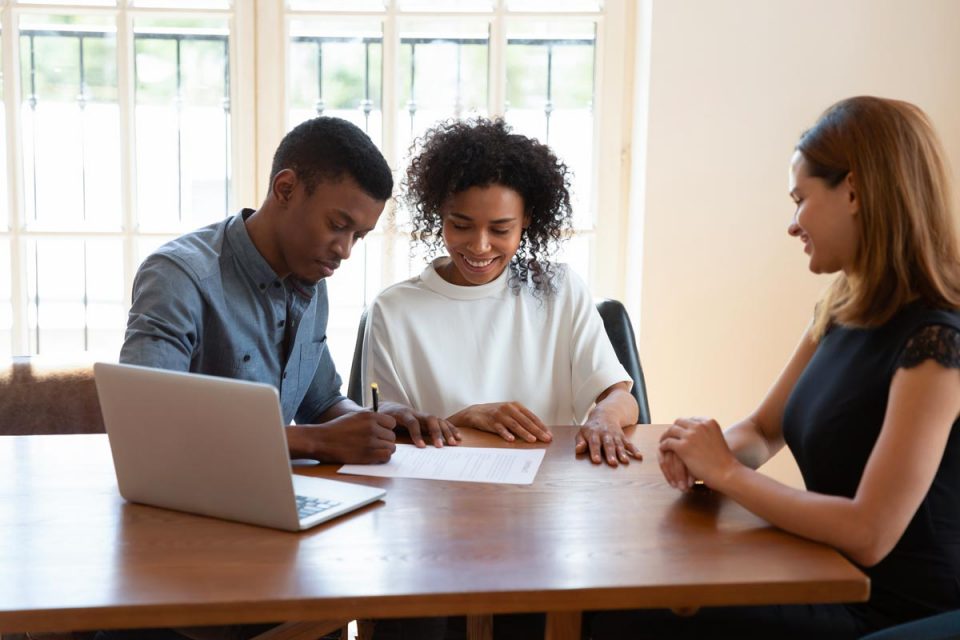 A home buyer at a closing table reviewing mortgage and title documents with a pen and a folder on the table, natural indoor light, real photography style