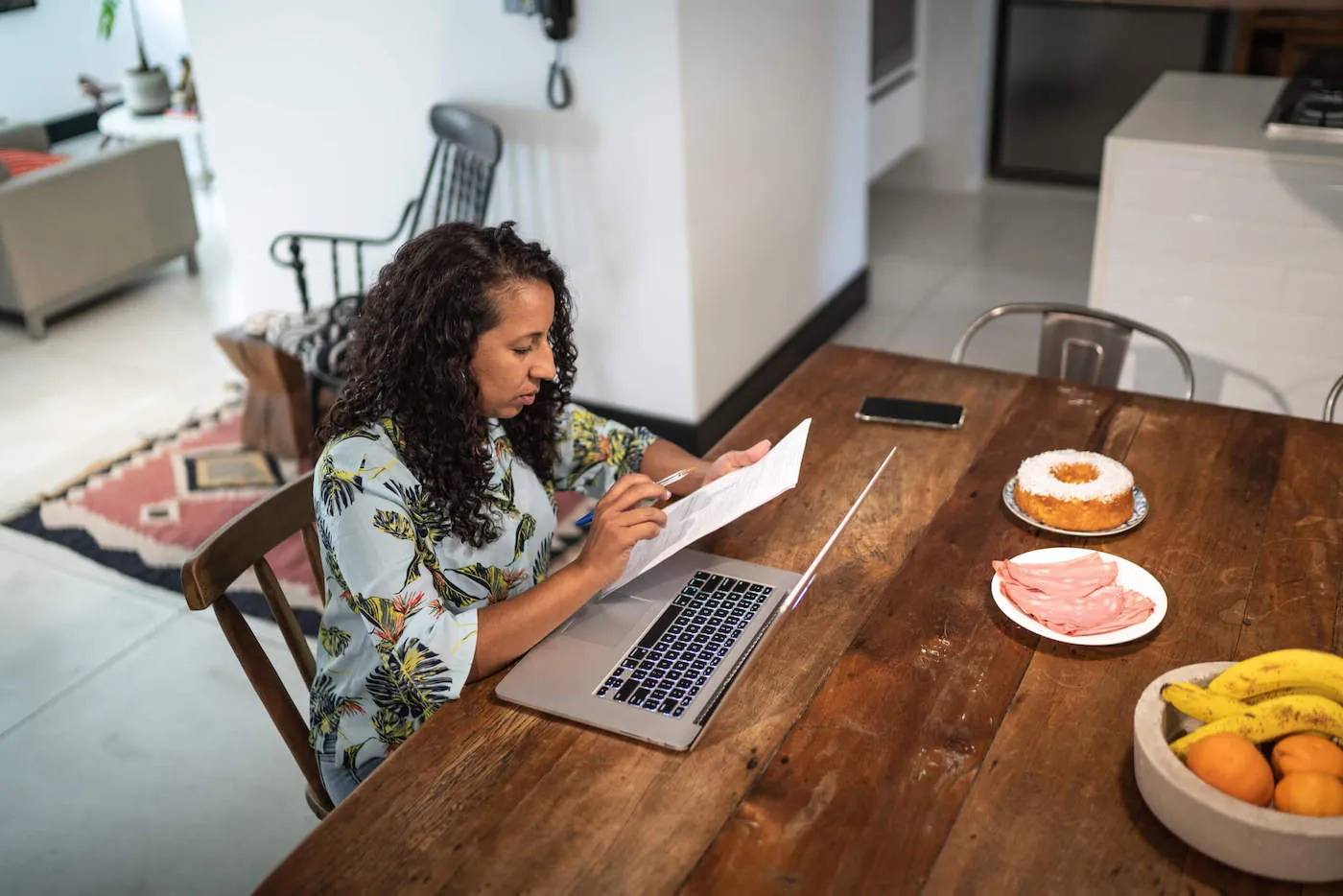 A homebuyer sitting at a kitchen table reviewing mortgage paperwork with a calculator and a laptop, candid real-life photo