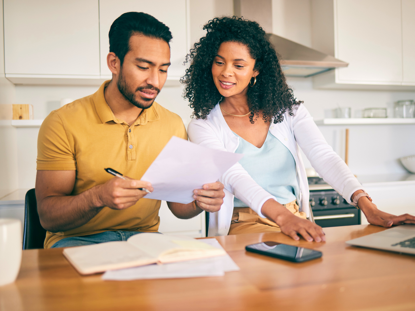 A homeowner signing mortgage paperwork at a kitchen table with a calculator and a laptop nearby, natural indoor light, realistic photo