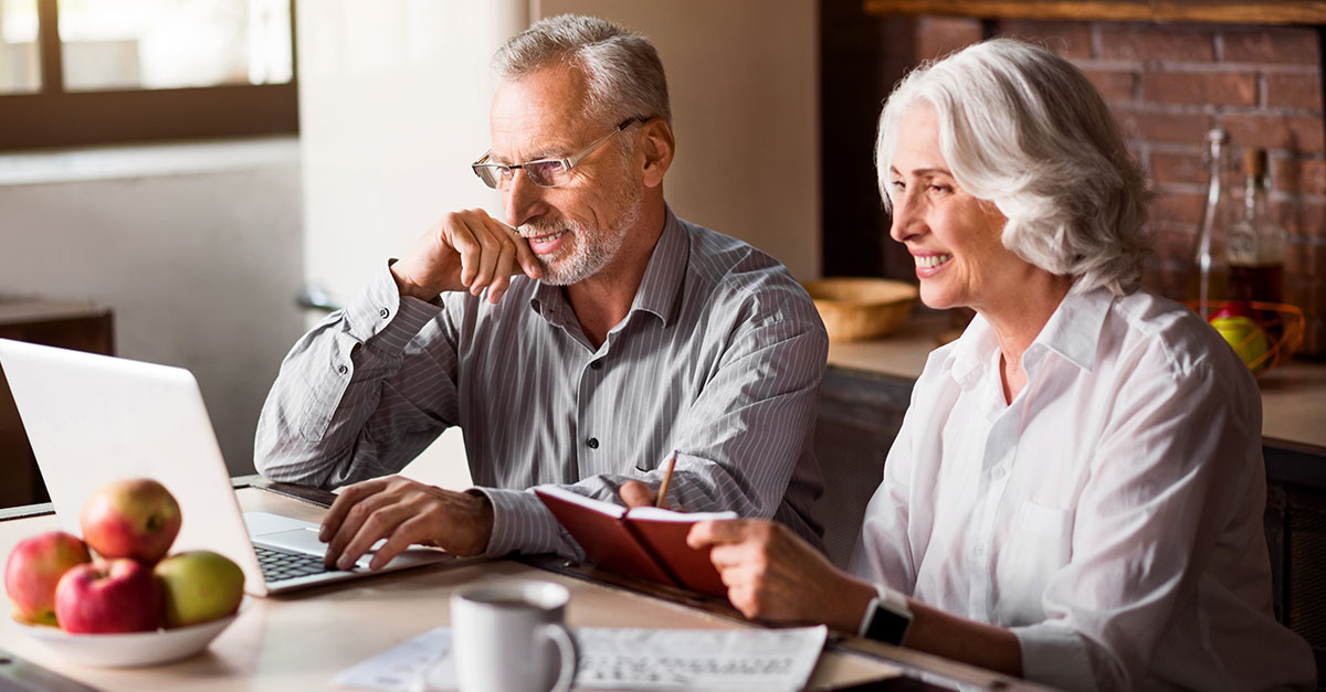 A married couple sitting at a dining table reviewing tax documents and a laptop together in a calm home setting, documentary photography style