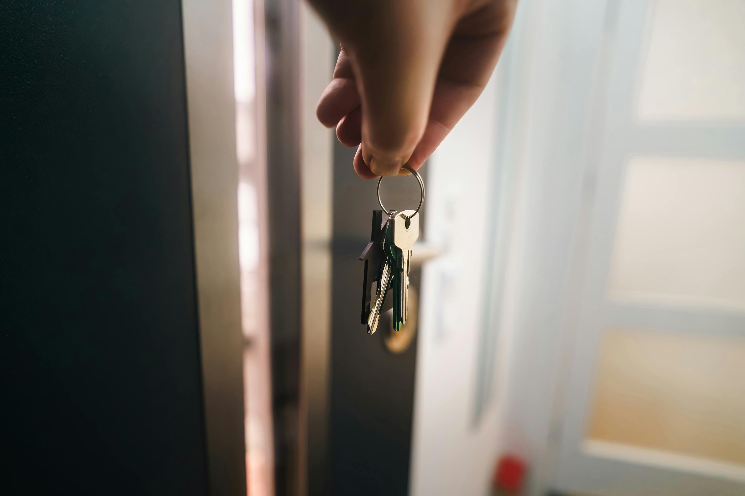 A new homeowner holding a set of house keys while standing near the front door of a recently purchased home in daylight, realistic photography