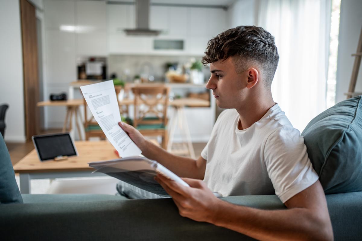 A parent and college-aged student sitting at a kitchen table reviewing loan paperwork with a laptop and a calculator, natural indoor light, candid photo
