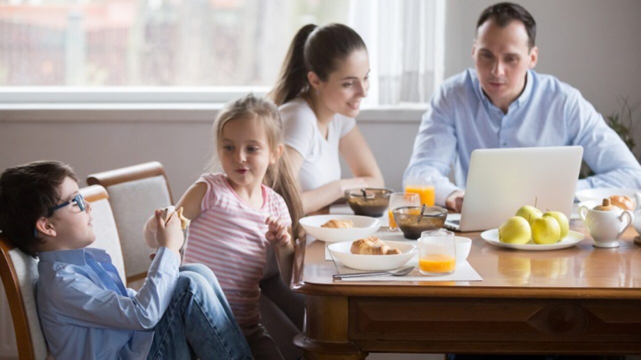 A parent sitting at a kitchen table reviewing college savings account paperwork and a laptop budget spreadsheet in warm evening light, realistic photo