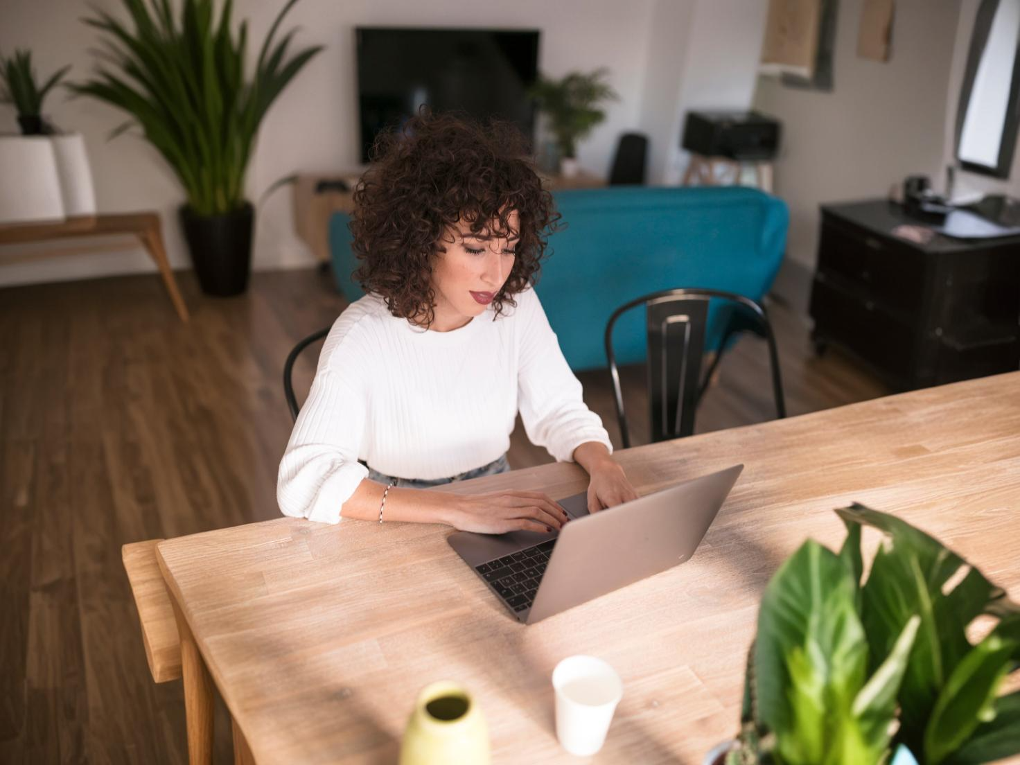 A person at a home desk organizing paperwork and writing notes in a notebook next to a laptop, realistic photo