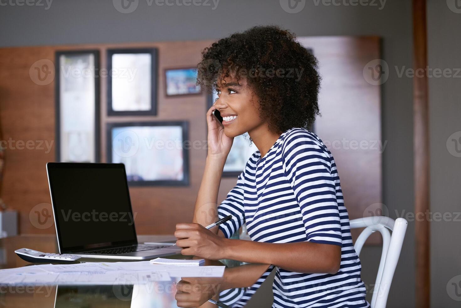 A person at home holding a smartphone to their ear while looking at a laptop with a bank website open, real photo