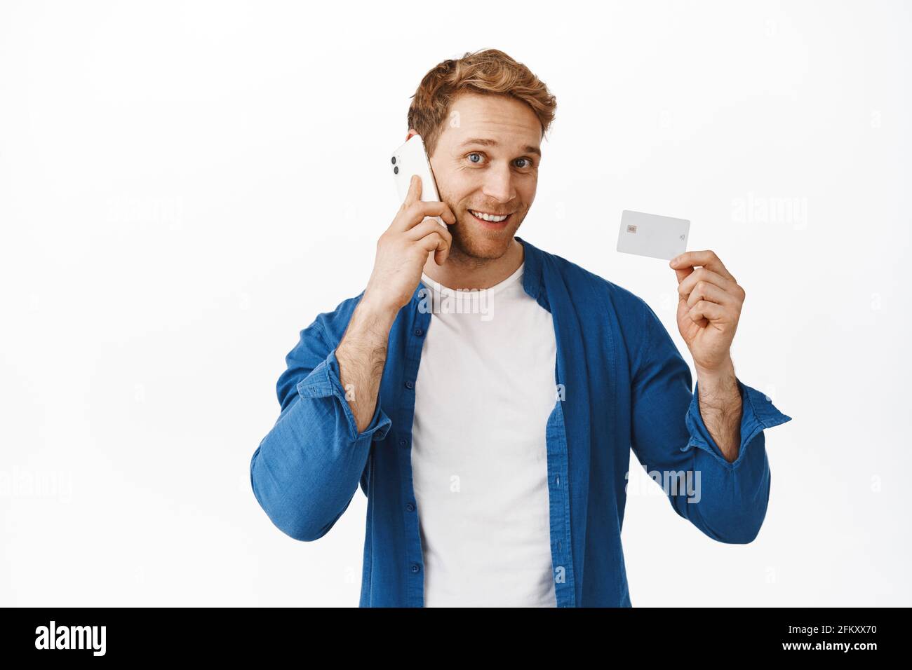 A person holding a credit card while talking on a smartphone at a desk, with a notepad open and a calm focused expression, real photography style