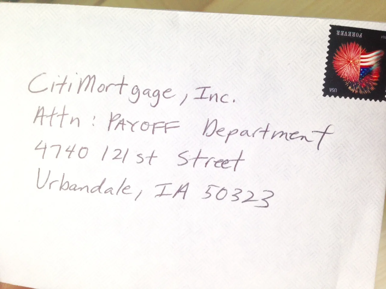 A person holding a printed loan payoff letter while sitting at a table with a stamped envelope and a pen