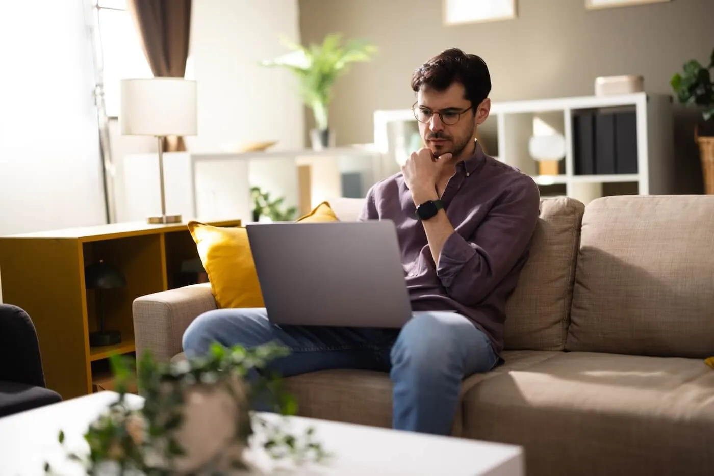 A person in a living room reviewing a credit report on a laptop with printed pages on the coffee table, realistic photography style