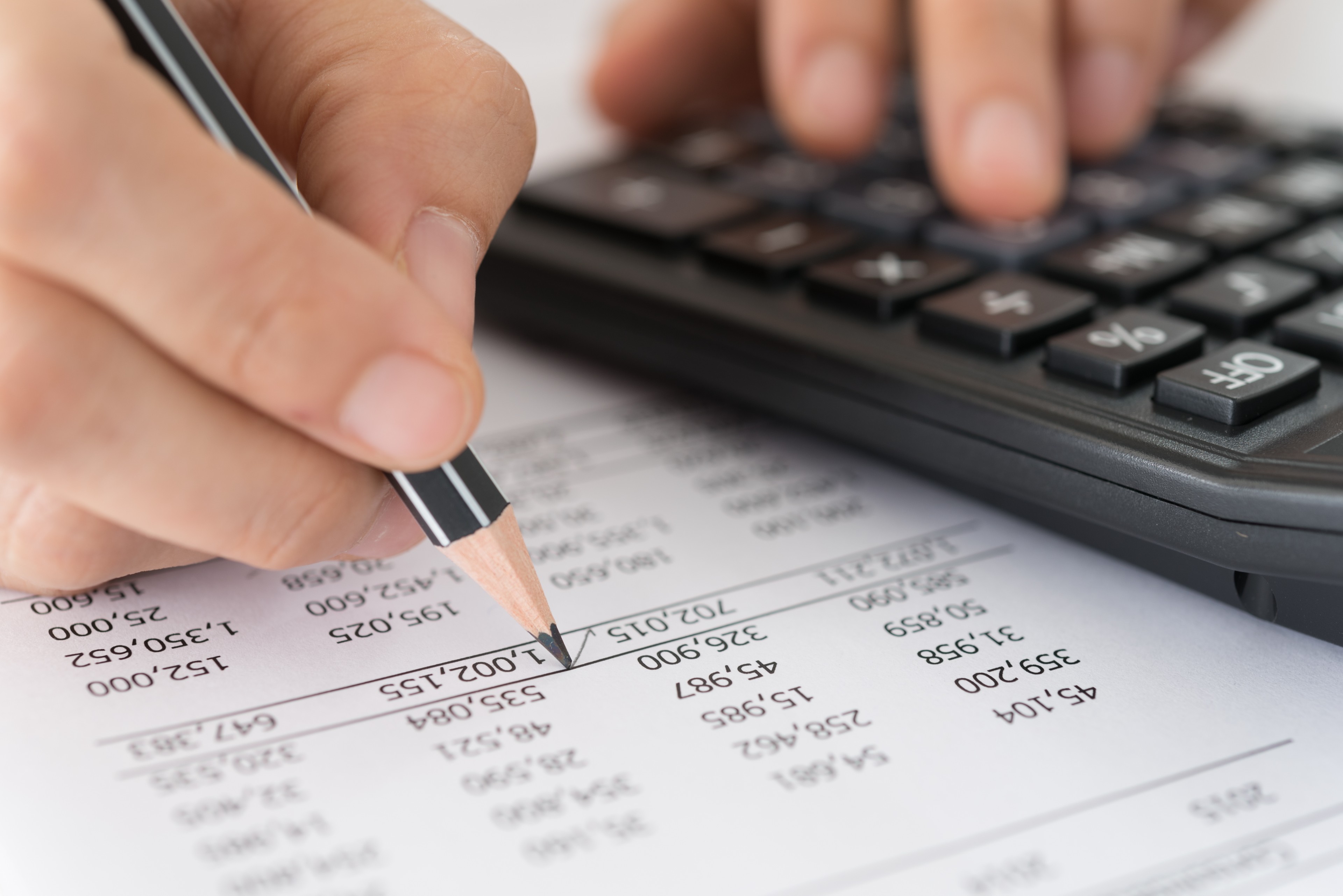 A person reviewing printed bank statements at a desk with a highlighter and a calculator, focusing on personal finance paperwork