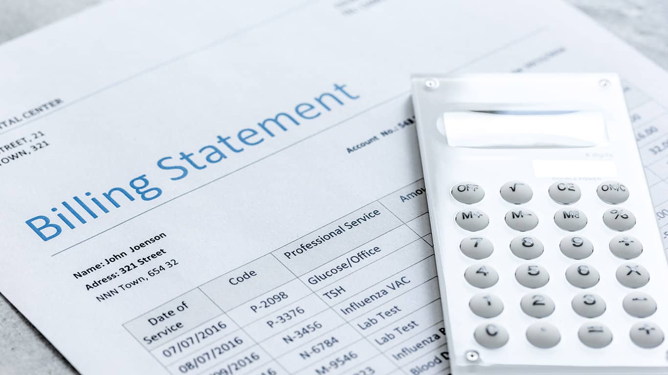 A person sitting at a dining table reviewing medical bills and an insurance statement with a calculator nearby