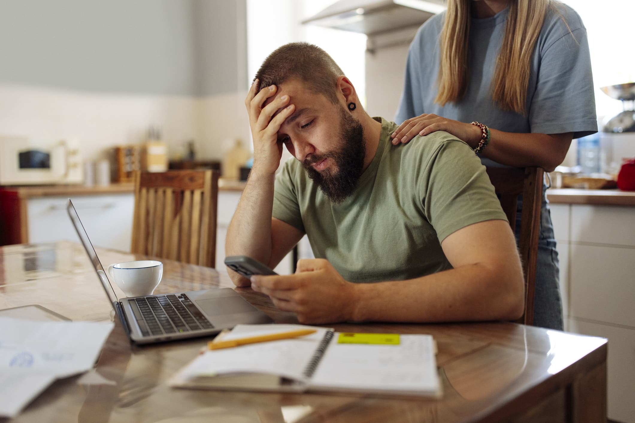 A person sitting at a home office desk talking on the phone while viewing a student loan account on a computer monitor, candid realistic photo