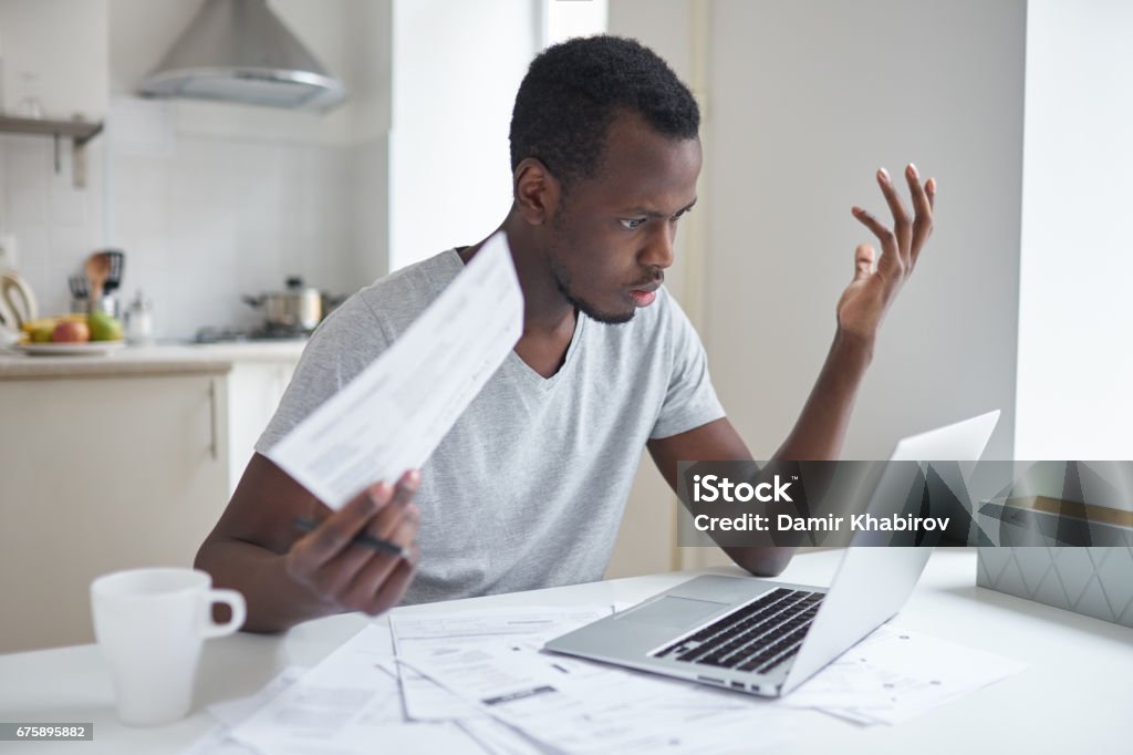 A person sitting at a kitchen table paying monthly bills on a laptop with a notebook and debit card nearby, realistic photo