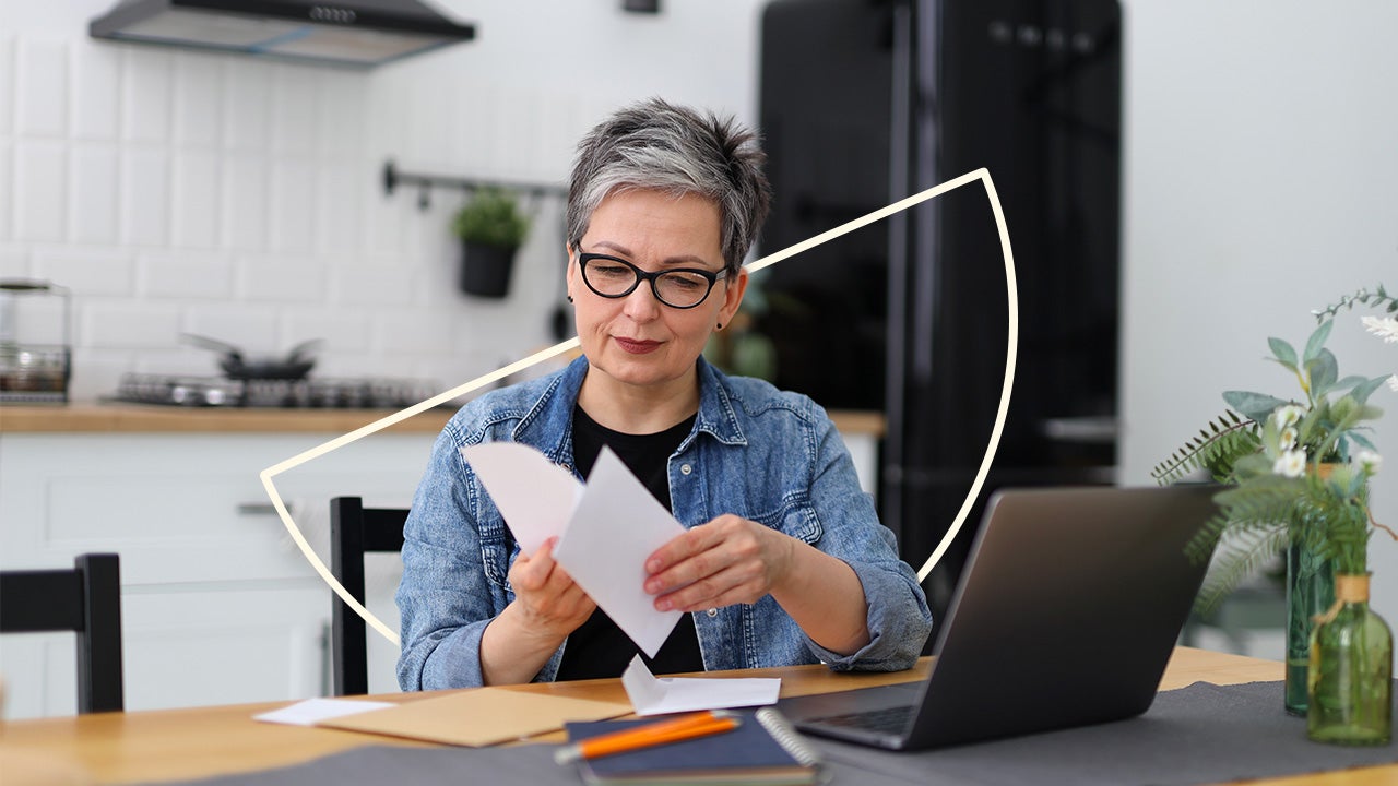 A person sitting at a kitchen table reviewing a credit report on a laptop with a notebook and a cup of coffee nearby, candid real-life photo