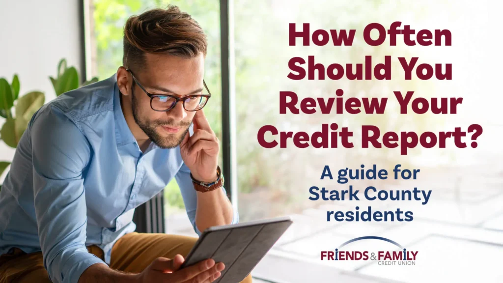 A person sitting at a kitchen table reviewing a credit report on a laptop with papers spread out, realistic photo