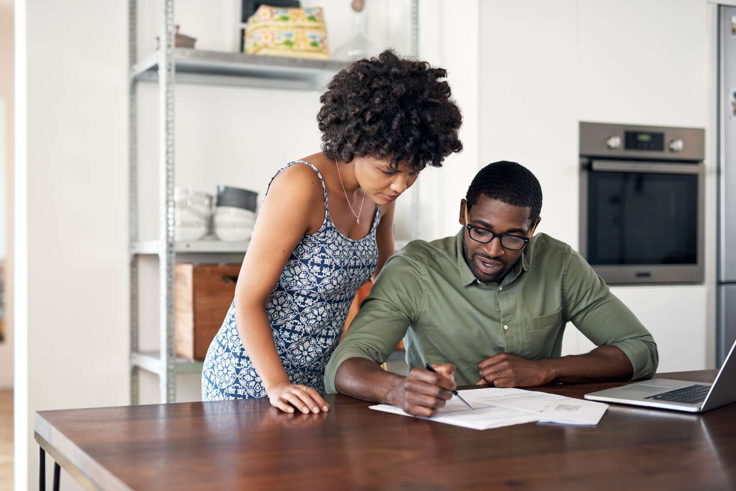A person sitting at a kitchen table reviewing car insurance policy documents next to a laptop and a set of car keys, natural indoor light, real photo style
