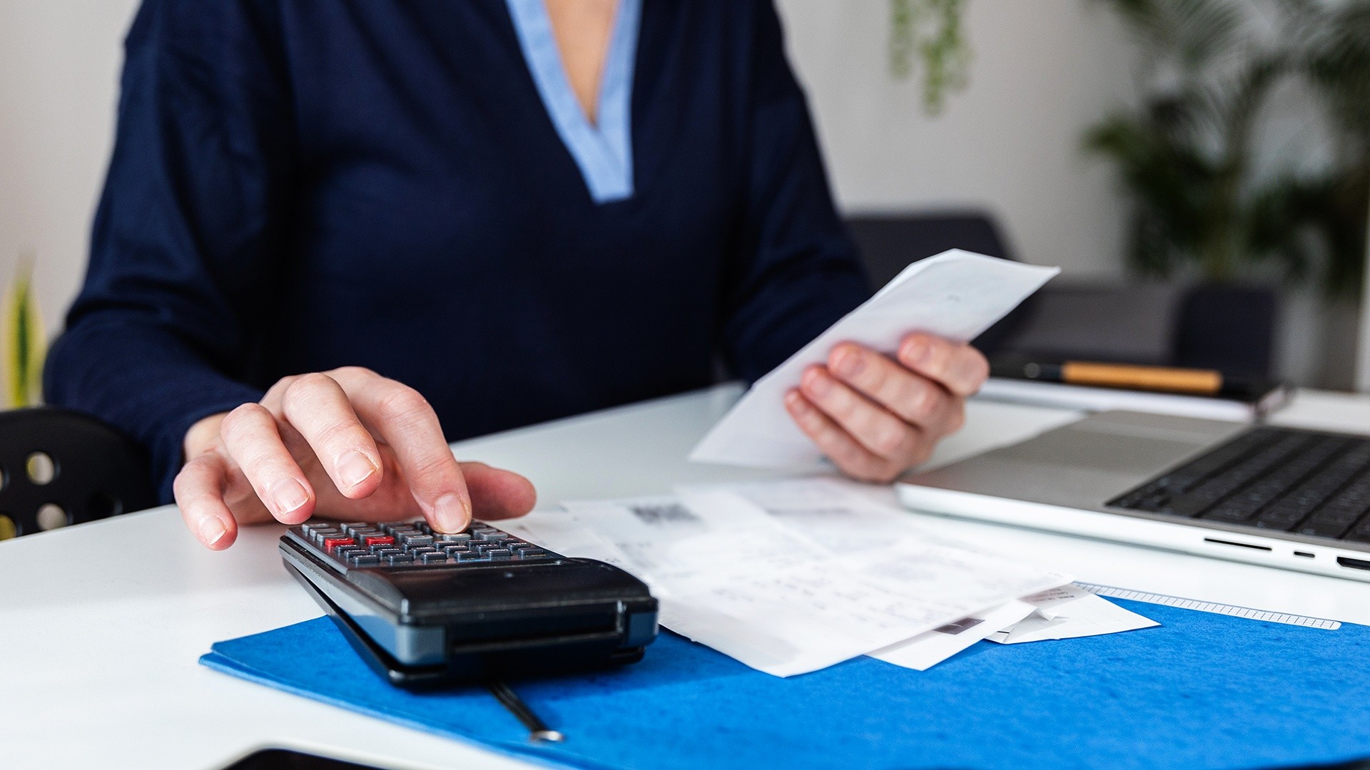 A person’s hands using a calculator beside a credit card and a handwritten budget notebook on a desk, realistic photo