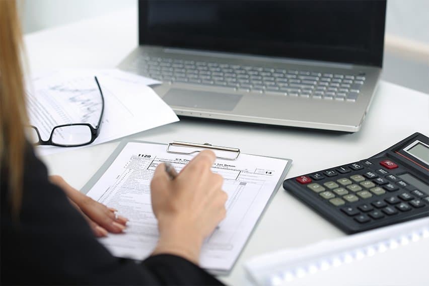A real employee sitting at an office desk filling out a W-4 form with a pen next to a laptop and a pay stub, natural light, documentary photography style