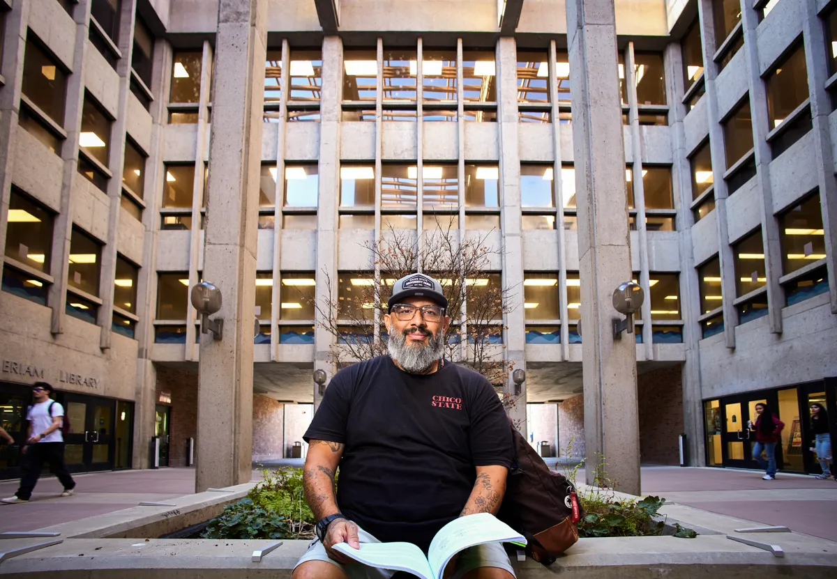 A real-life photo of a person holding a small stack of mail while standing near an apartment building entrance, representing address history and identity details