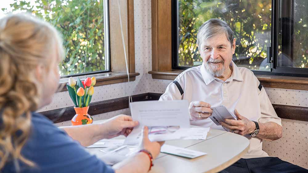 A real-life photo of an adult sitting at a kitchen table reviewing printed credit report pages with a laptop and a pen nearby, candid indoor lighting