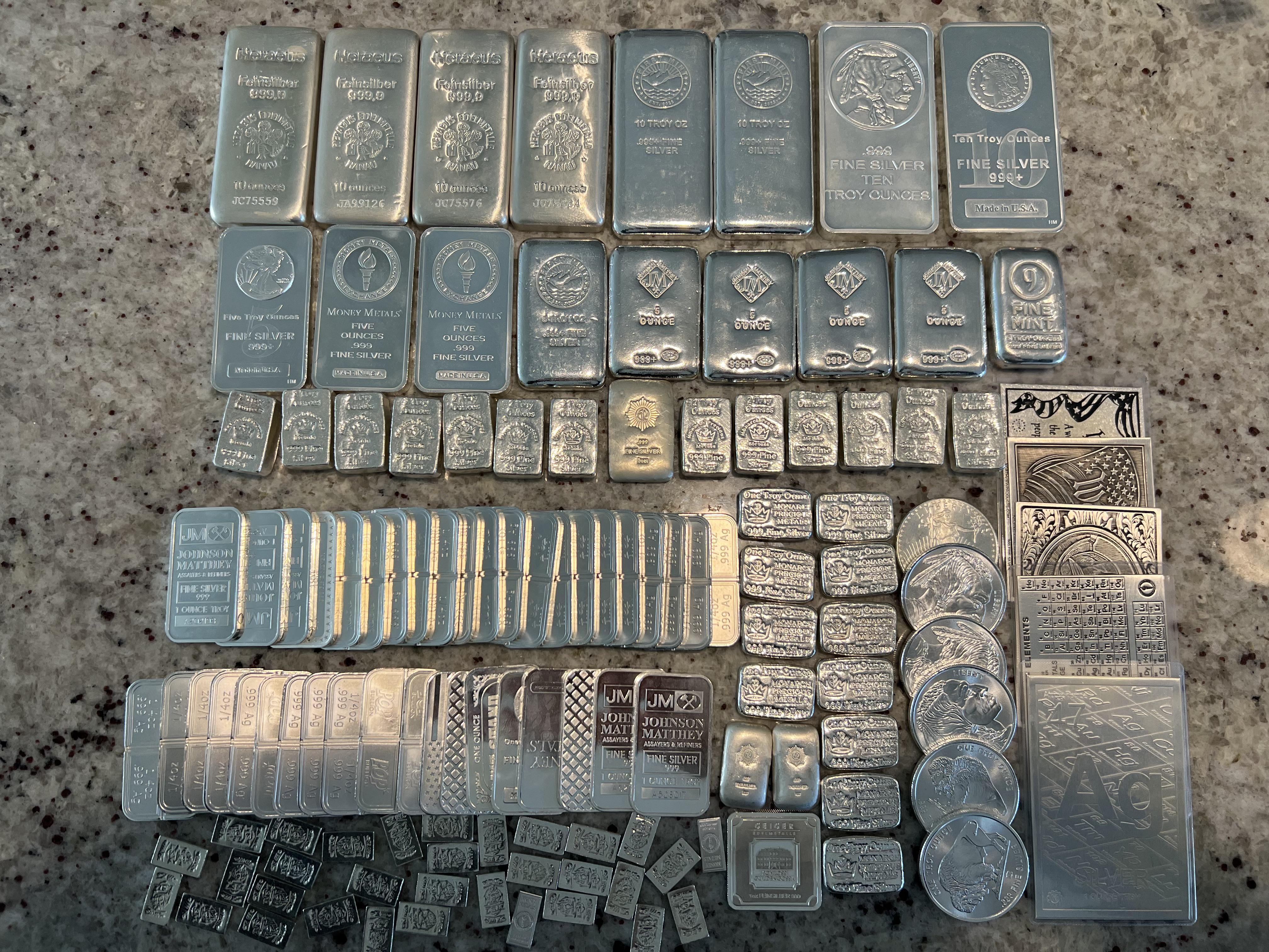 A real photograph of stacked silver bullion bars on a wooden tabletop with soft natural light