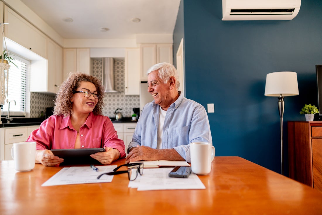 A retired couple sitting at a kitchen table reviewing retirement account paperwork with a laptop open, natural light, real-life photo