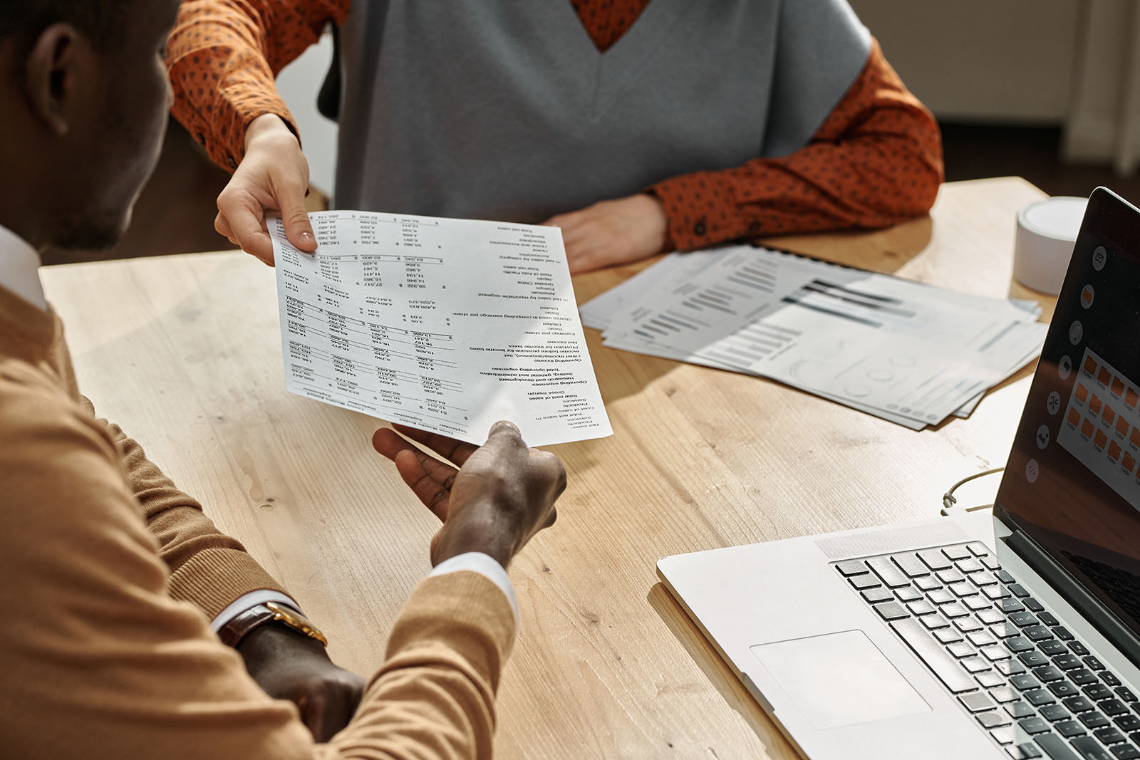 A salaried employee sitting at a kitchen table reviewing a printed bonus pay stub next to a laptop, realistic photography style
