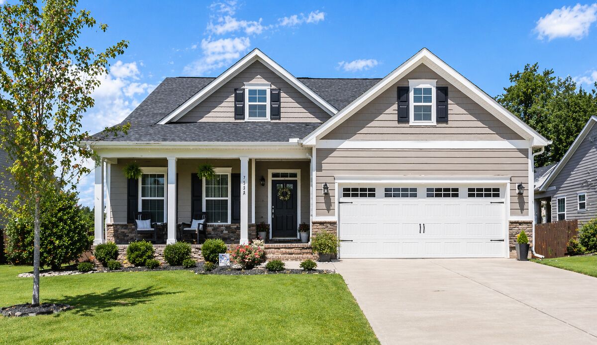 A single-family home in a quiet suburban neighborhood on a clear day, photographed from the sidewalk with a driveway and front porch visible