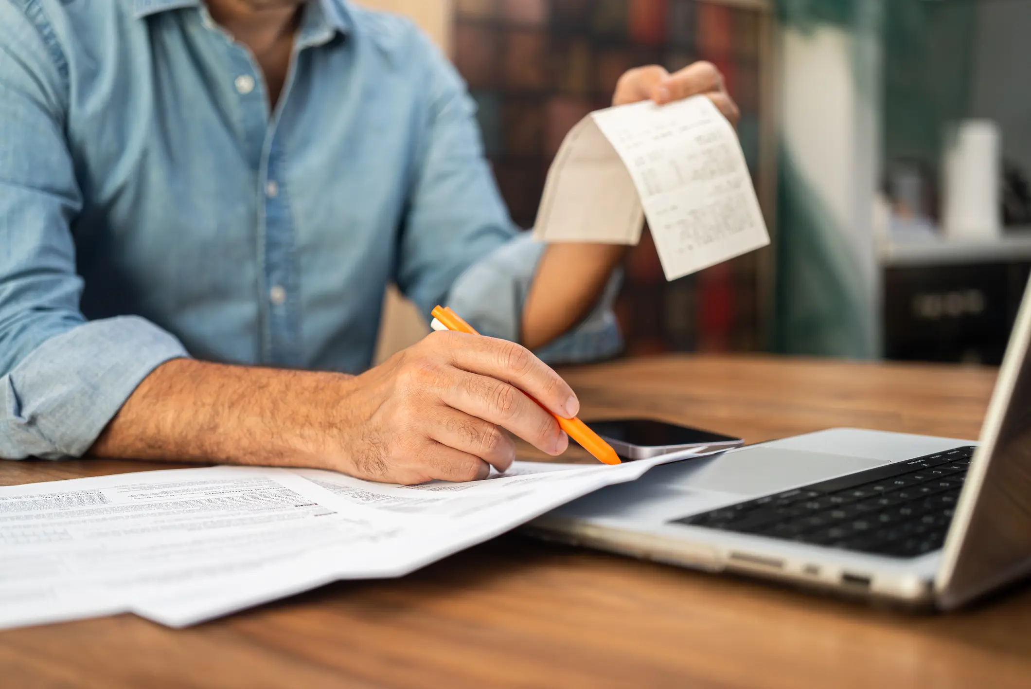 A small business owner sitting at a desk sorting paper receipts next to a laptop and a coffee mug, real photography style