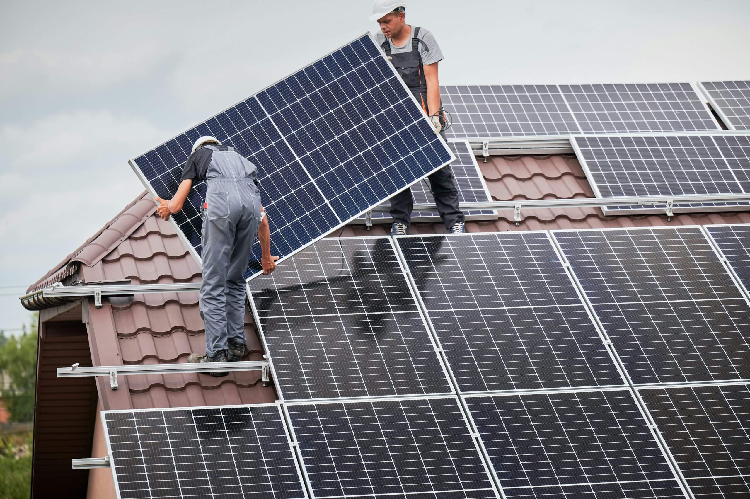 A solar installer standing on a residential roof in daylight while securing solar panels to mounting rails, real photo