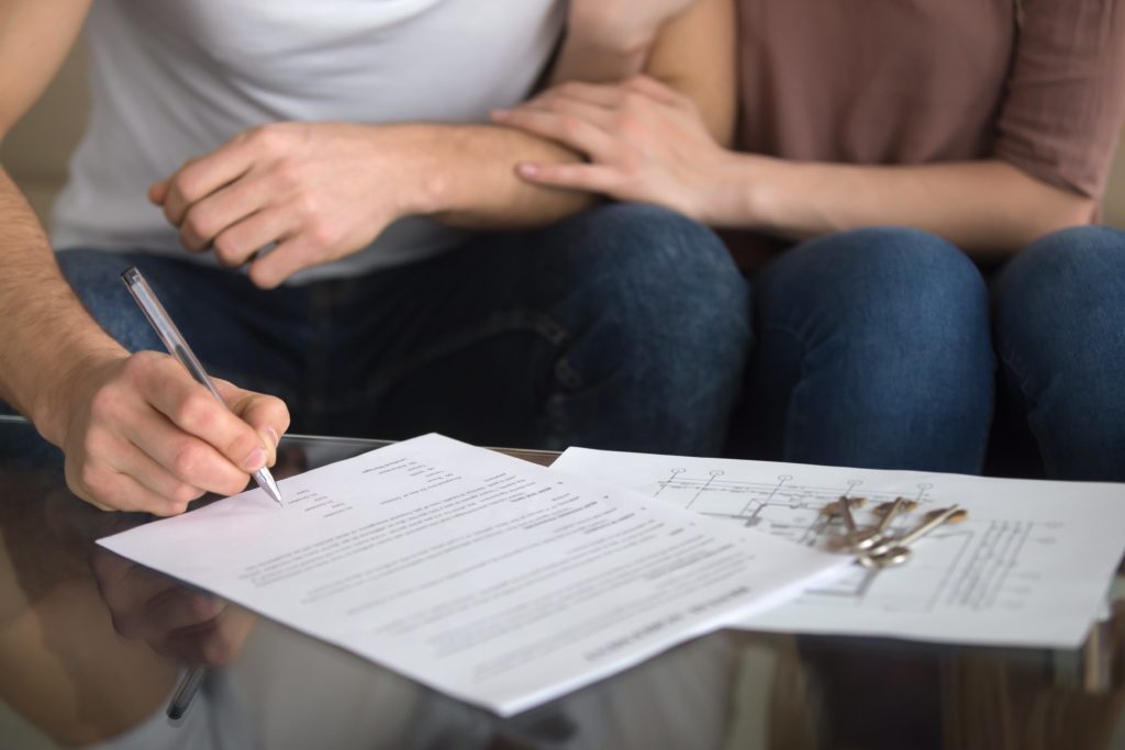 A stack of home closing documents with a pen and a house key resting on top of the paperwork