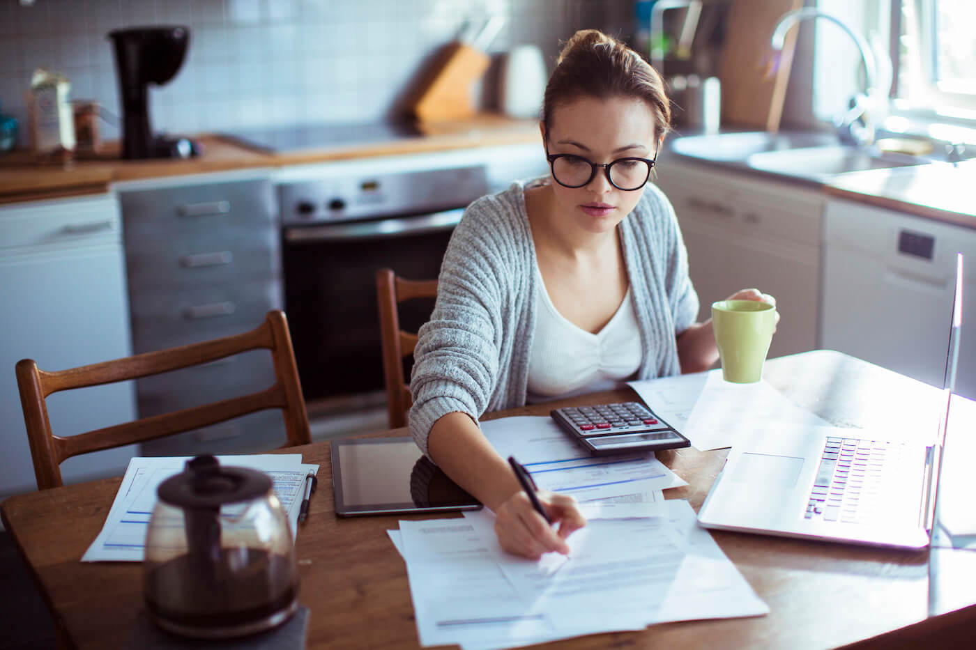 A student loan borrower sitting at a kitchen table reviewing federal loan paperwork and a laptop account screen, candid home photography style