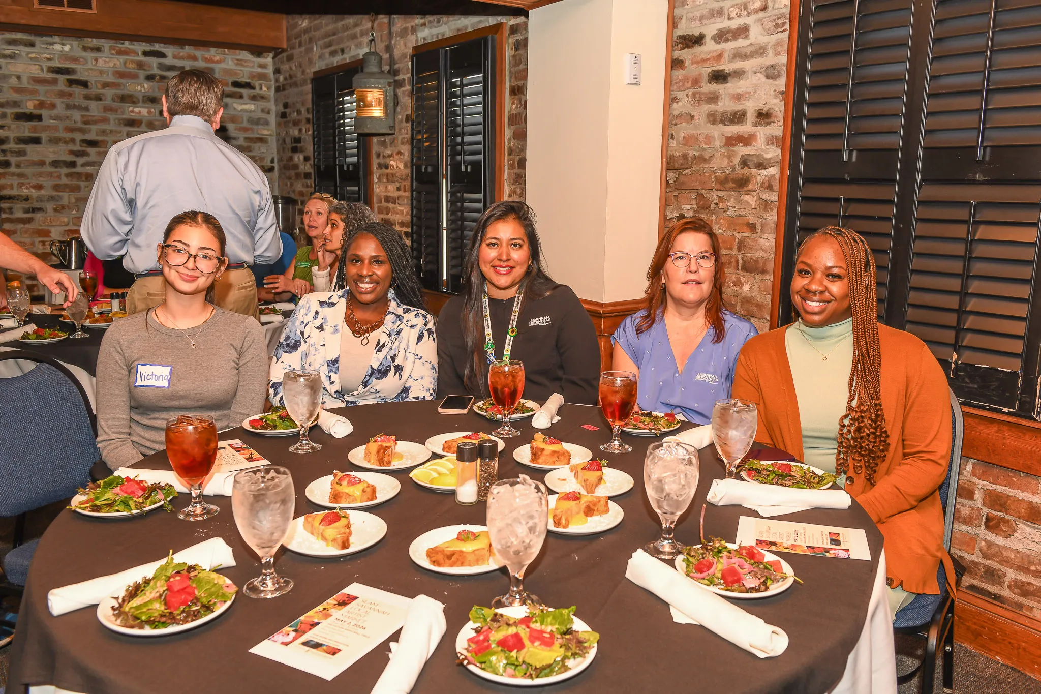 A teacher at a kitchen table signing student loan paperwork with a pen next to a laptop and a mug, candid realistic photography