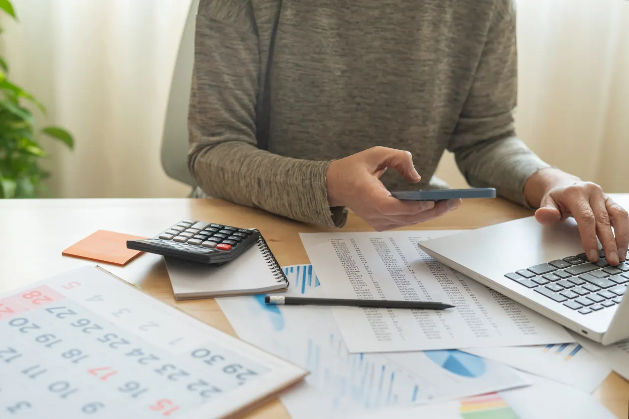 A young adult sitting at a desk reviewing bills with a calculator and a notebook, realistic indoor photo