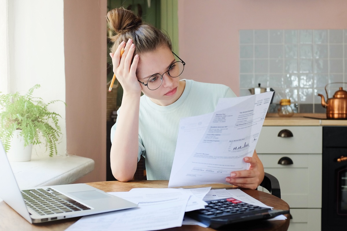 A young adult sitting at a kitchen table in the evening, reviewing student loan statements and a laptop budget sheet, realistic documentary photo
