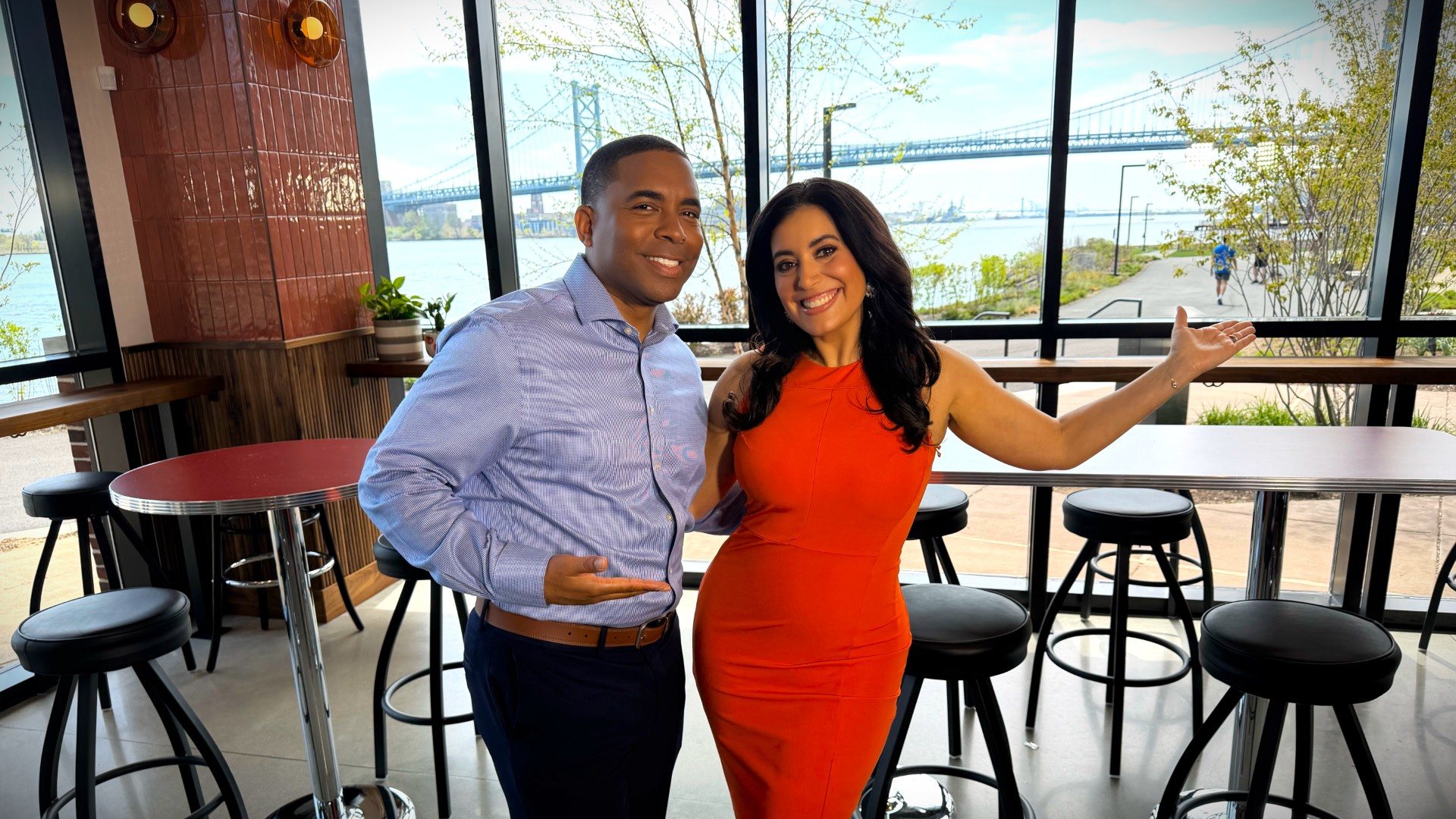 An adult sitting at a kitchen table holding a phone while looking at a utility bill and a notebook, realistic indoor photograph
