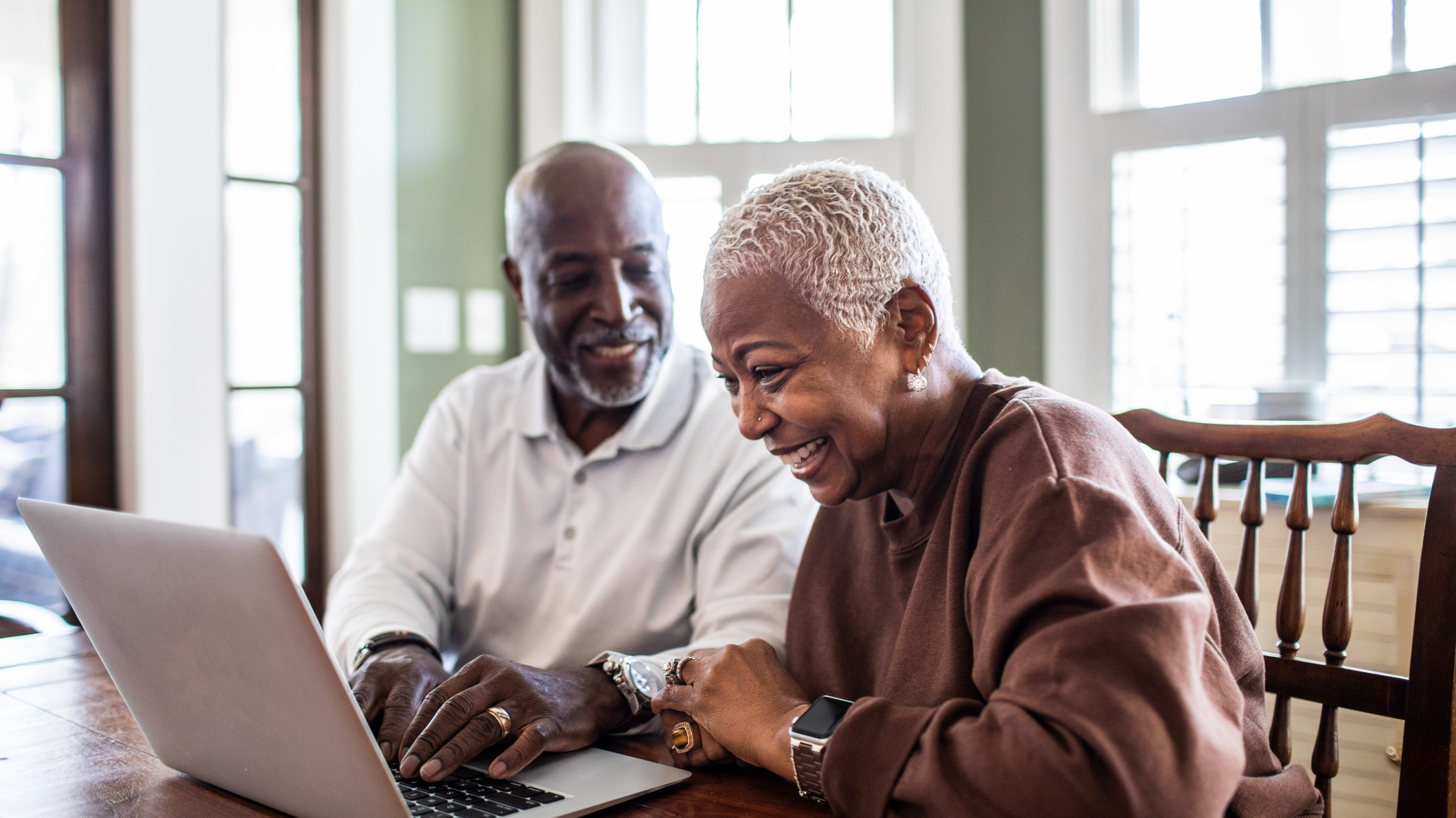 An older adult sitting in a living room chair opening retirement account mail and reviewing papers, natural window light
