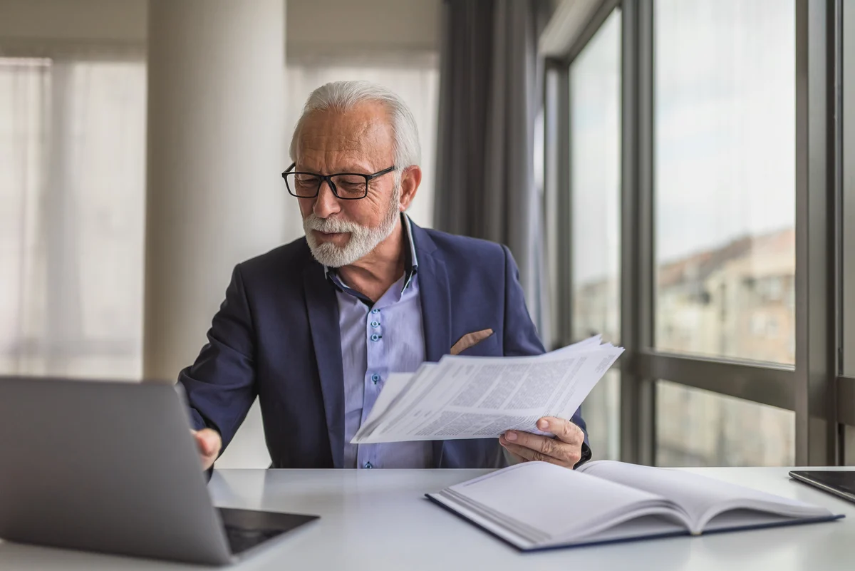 An older man in a home office logging into a retirement plan website on a laptop, focused expression, real-life photo